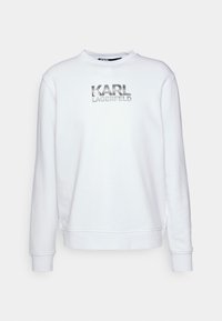 Weißes Sweatshirt mit Rundhalsausschnitt und gerippten Bündchen, mit einem metallic silbernen "KARL LAGERFELD" Logo in der Mitte auf der Vorderseite.