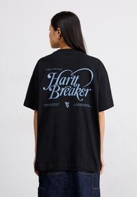 Camiseta de algodón negra con grandes gráficos azules en la parte posterior que dicen "Hart Breaker". El diseño incluye mangas cortas y un corte holgado.