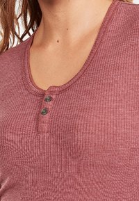 Mauve ribbed henley-paita, jossa on pyöreä pääntie, kolme napin aukkoa ja rakenteellinen kangas lisäyksinä.