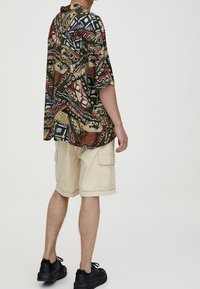 Camisa de manga corta, con un patrón en colores marrón, azul y beige, combinada con unos pantalones cortos tipo cargo en color crema y zapatillas negras.