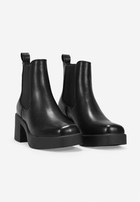 Botas de cuero negro hasta el tobillo con paneles laterales elásticos, puntera redondeada y tacón cuadrado. Presentan una textura suave y una lengüeta trasera.