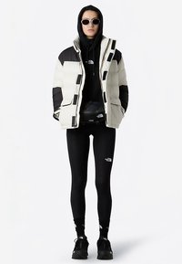 Puffer jacket in cream and black with a zip closure, layered over a black hoodie, paired with black leggings and sneakers.