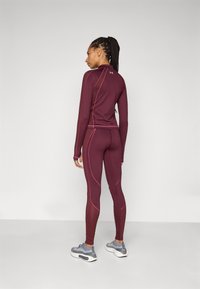 Burgunderrød treningstopp og tights med rosa sømmer, sammen med grå joggesko. Har en tettsittende design og lange ermer.
