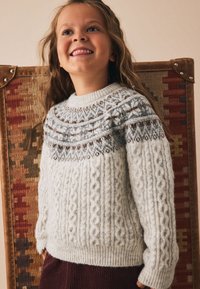 Cream-colored knitted sweater featuring a textured cable pattern, patterned yoke in grey, brown, and white. Ribbed cuffs and hem.