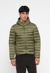Jachetă puffer verde măslin cu glugă, având matlasare orizontală, fermoar frontal și două buzunare laterale. Sigla Lacoste pe piept.