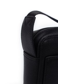 Borsa in pelle nera con texture, dotata di una zip superiore e un manico corto. L'esterno presenta una finitura effetto granulato con accenti rettangolari minimalisti.