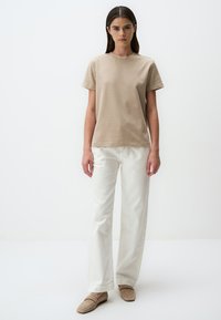 T-shirt in cotone beige a maniche corte, abbinato a jeans bianchi a gamba dritta e mocassini beige. Design semplice e classico con una texture leggera.