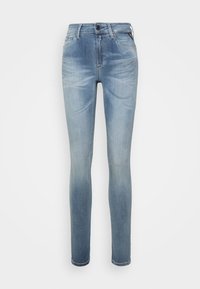 Jeans skinny azzurri chiari con effetto di lavaggio sbiadito e design a cinque tasche su uno sfondo bianco semplice.