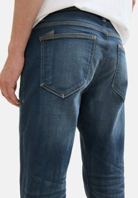 Sötétkék farmernadrág enyhén kopott hatású textúrával, két hátsó zsebbel és kontrasztos varrással a varrásvonalakon.