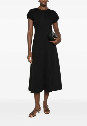 Donna che indossa un vestito midi nero con maniche corte, tiene una pochette nera e indossa sandali neri con cinturini e tacco basso.