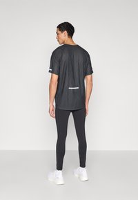 Camiseta deportiva negra con tejido texturizado, mangas cortas y detalles reflectantes, combinada con leggings negros y zapatillas blancas.