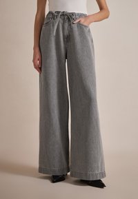 Pantalons en denim gris à jambes larges avec un cordon de serrage à la taille et des poches latérales, présentant une texture douce et une coupe droite et décontractée.