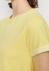 T-shirt jaune à manches courtes avec un col ras du cou, présentant une texture lisse et une finition blanche contrastante au niveau des manches, exposé de côté.