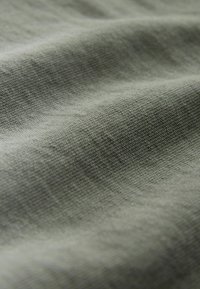 Light green textured fabric with visible weave pattern; folds create soft shadows, indicating a lightweight, breathable material.