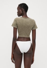 Haut court côtelé vert olive avec des manches courtes, associé à un bas de bikini côtelé blanc taille haute. Vue de dos, texture lisse et design ajusté.