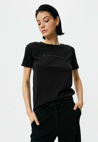 Sort kortærmet t-shirt lavet af bomuld, med teksten "Gør det, du elsker" i et subtilt design over brystet.
