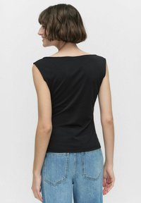 Svart ärmlös topp med rund halsringning, tillverkad av mjuk tyg, figurnära design, kombinerad med ljusblå hög midja denimjeans.