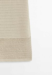 Tissu crochet beige avec une section supérieure tissée plus serrée et un motif à tissage ouvert plus lâche en bas.