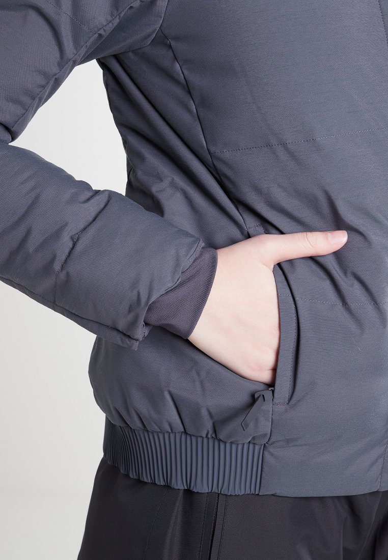Chaqueta acolchada gris con dobladillo acanalado y bolsillos laterales. Presenta un exterior suave y puños elásticos para un ajuste ceñido.