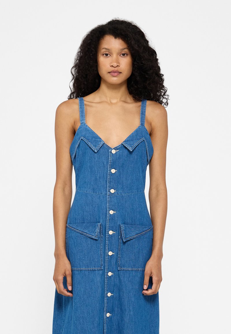 Denim kleita ar pieguļošu bodi, platām siksnām, smailu apkakli un priekšējo pogu aizdari. Kabatas ar kontrastējošiem šuvju punktiem.