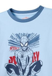 Lichtblauwe katoenen t-shirt met een spinnenafbeelding met zwarte contouren en rode tekst, ronde marineblauwe kraag en comic-stijl accenten.