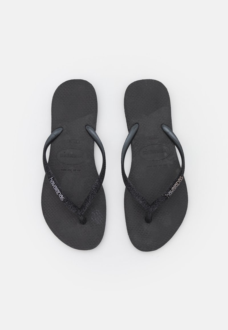 Tongs noires avec des semelles texturées, dotées de brides brillantes et d'un logo subtil sur la bride. Design simple et léger pour un port décontracté.