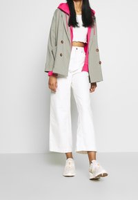 Giacca a scacchi houndstooth con cappuccio rosa, top bianco corto, pantaloni bianchi a gamba ampia e sneakers chiare con accenti crema e gialli.