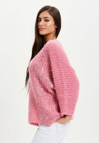 Pink knitted sweater with a loose fit, featuring silver sequins and wide sleeves, showcasing a textured pattern.
