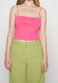 Upnutý, jasně růžový top na tenkých ramínkách, spárovaný s světl zelenými širokými kalhotami s záhyby a bočními kapsami.