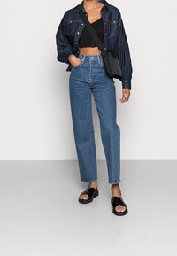 Modré džíny s vysokým pasem, černý crop top, tmavě modrá oversized košile a černé sandály. Jednoduchý design s uvolněným střihem.