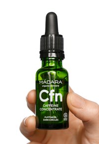 Grön glasdroppflaska märkt "Cfn Koffein Koncentrat", svart droppartopp och innehåller text om fördelar för puffer hud.
