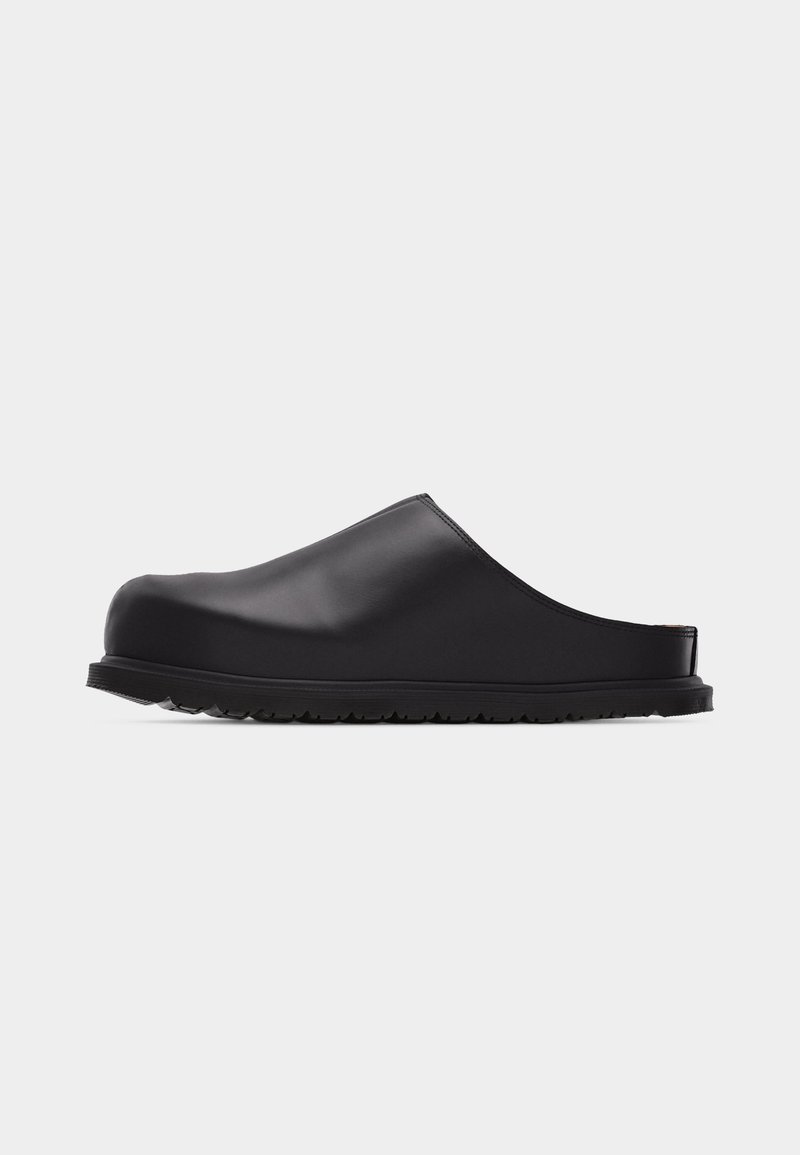 Zoccolo nero slip-on con punta chiusa, tomaia liscia e suola rigata, mostrato di profilo su sfondo bianco.