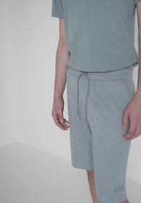 Pantaloni corti in cotone grigio chiaro con superficie texturizzata, vita elastica e cordino regolabile. La maglietta grigia a maniche corte completa il look.