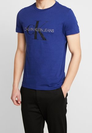 Blaues Baumwoll-T-Shirt mit Rundhalsausschnitt und kurzen Ärmeln, vorne mit einem schwarzen Calvin Klein Jeans-Logo bedruckt.
