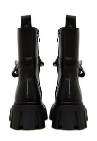 Bottes chevilles en cuir noir avec une semelle épaisse, dotées d'une tige haute, d'une fermeture éclair et de nœuds décoratifs sur les côtés.