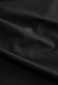 Tissu noir avec un motif hexagonal texturé. Le matériau semble lisse avec un léger éclat, tombant doucement et montrant de légers plis.