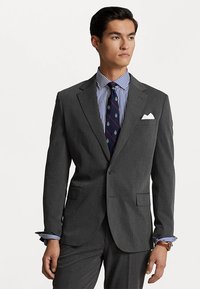 Grijze blazer met notch-revers, twee voorkruiken, gecombineerd met een blauw-wit gestreept overhemd en een patroonstropdas. Witte pochet detail.