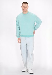 Mintgroene sweatshirt met een ronde halslijn, gecombineerd met lichtblauwe cargobroek met zijzakken, gedragen met witte sneakers.