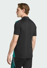 Polo shirt de sport noir avec des accents turquoise sur les épaules, coupe slim, manches courtes et texture de tissu lisse.