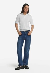 Vit kortärmad polo med krage, i kombination med blå raka jeans och svarta loafers. Outfiten har en slim fit och en minimalistisk design.