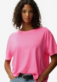 Lyserød oversized t-shirt lavet af letvægtsstof med rund hals og korte ærmer, med minimal branding og en afslappet pasform.