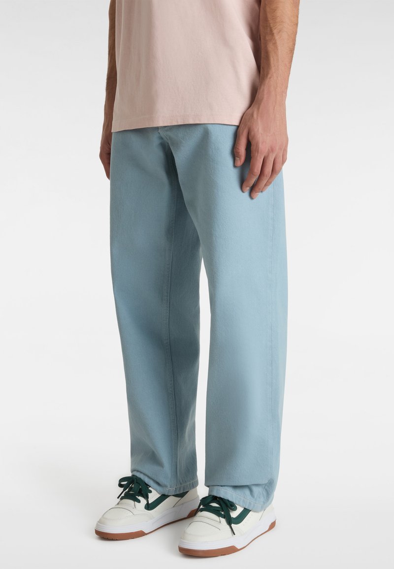 Light blue wide-leg pants made of denim, feature a smooth texture and subtle stitching. Paired with white and green sneakers.