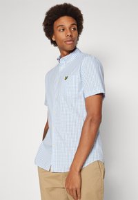 Short-sleeve, light blue gingham shirt with a button-down collar, featuring white buttons and a small yellow logo on the chest pocket.
