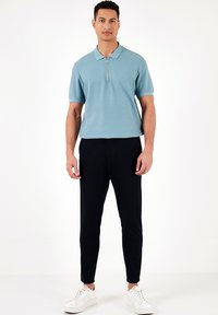 Gai zilas īsām piedurknēm polo krekls ar pusi rāvējslēdzēju, valkāts ar melnām pieguļošām biksēm un baltām sporta kurpēm. Gluda tekstūra, ikdienišķs dizains.