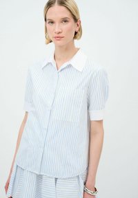 Camicetta a maniche corte con bottoni realizzata in tessuto leggero, con strisce verticali blu e bianche, colletto bianco e una tasca sul davanti.