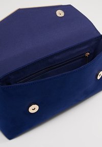 Bolso de ante azul marino con cierre magnético y herrajes en tono dorado. Cuenta con un bolsillo interior con cremallera para mayor organización.
