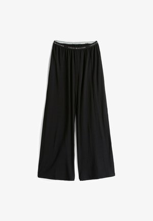 Zwarte wijde broek van zacht materiaal, met een elastische tailleband waarop de merknaam "Tommy Hilfiger" in het wit is gedrukt.