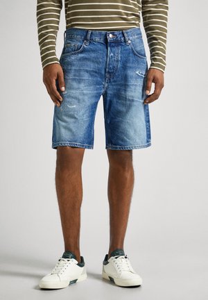 Shorts de mezclilla en azul claro con detalles deshilachados, con un diseño clásico de cinco bolsillos y un corte regular, combinados con zapatillas blancas.