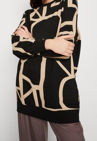 Felpa nera con motivo astratto beige. Presenta maniche lunghe, polsini a coste e una vestibilità comoda. Tessuto morbido con una superficie liscia.