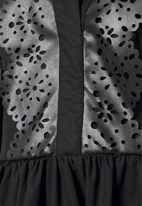 Svart klänning med ett texturerat läderliv med blommig utskärning och en rynkad kjol.